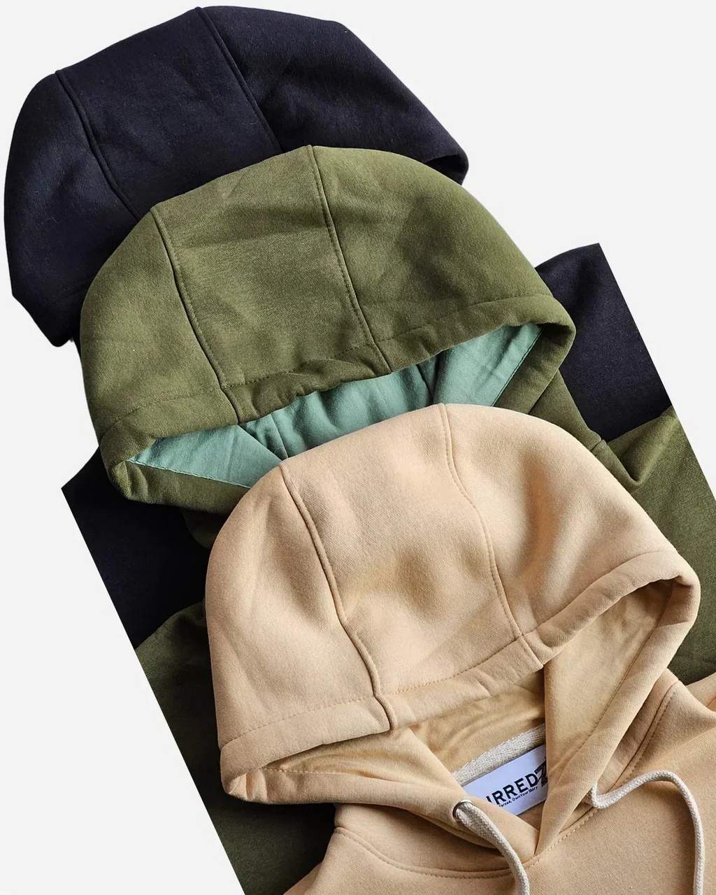 Stacked hoodies in beige, olive green, and black on a white background